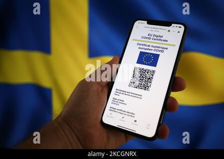 An EU COVID certificate is seen on a mobile device in with a Swedish flag in the background in this photo illustartion in Warsaw, Poland on July 1, 2021. The EU COVID certificate, a document in digital or analogue form that allows fully vaccinated people to travel to all 27 EU member states has become avaialbe since July 1. (Photo by STR/NurPhoto) Stock Photo