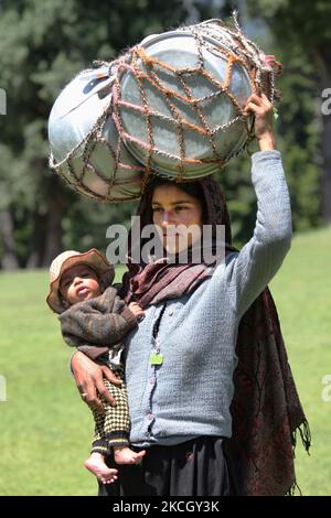 Nomadic Bakharwalli woman carries a large bundle of pots and pans on her head and her child in her arms as she prepares to relocate in Pahalgam, Kashmir, India. (Photo by Creative Touch Imaging Ltd./NurPhoto) Stock Photo