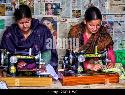Thakur girls working in a garment shop repair clothing with antique sewing machines, behind them plastered on the wall are newspapers with famous Bollywood film stars in Broat, Himachal Pradesh, India, on July 04, 2010. (Photo by Creative Touch Imaging Ltd./NurPhoto) Stock Photo