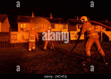 Members of the Fire Service dampen down nearby flats as close to a large bonfire during the Eleventh Night marking the start of the unionist Twelfth celebrations, in Craigy Hill, Larne. Tonight, large bonfires are lit in many Protestant loyalist neighbourhoods of Northern Ireland. Bonfires were originally lit to celebrate the Glorious Revolution (1688) and victory of Protestant king William of Orange over Catholic king James II at the Battle of the Boyne (1690), which began the Protestant Ascendancy in Ireland. On Monday, 12 July 2021, in Larne, County Antrim, Northern Ireland (Photo by Artur  Stock Photo
