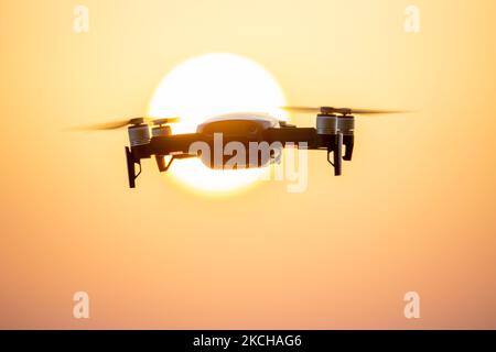 A quadcopter drone hovering during a flight in front of the sun. The flying drone is seen as a dark silhouette against the spectacular colorful sunset sky and the sun while the UAV is able to capture aerial videography and photography via a remote control. The specific drone is a DJI Mavic Air. The Unmanned aerial vehicle is popular for recreational usage by tourists as the technology is accessible to everybody in low cost but also has many professional applications Sani Beach area, Halkidiki, Greece on July 15, 2021 (Photo by Nicolas Economou/NurPhoto) Stock Photo