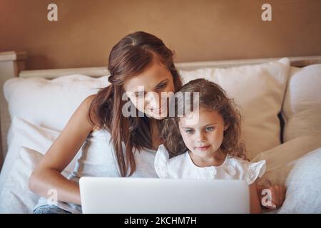 Technology makes learning more interesting and fun. a mother and her little daughter using a laptop together at home. Stock Photo