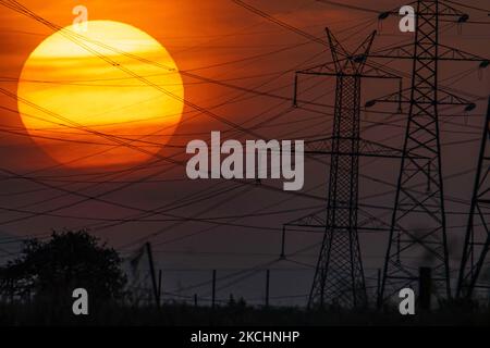 Summer sunset in Greece with electrical pylons near Thessaloniki city. High voltage electricity poles - towers during the sunset time in the magic hour. The metal towers as seen in the sunset in the Greek countryside, distribute electric energy from the power station where electricity is generated in coal production, across the country. The electric wires, the grid and pillars or power pylons are seen as silhouettes in the colorful cloudy dusk evening sky. Oreokastro, Thessaloniki in Greece on July 25, 2021 (Photo by Nicolas Economou/NurPhoto) Stock Photo