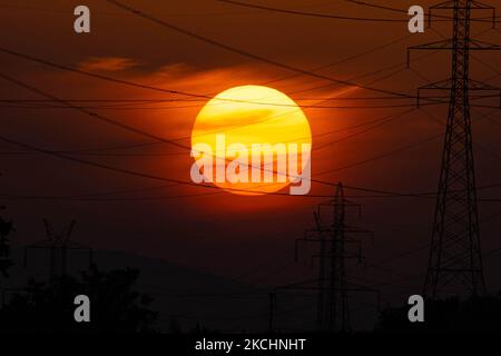 Summer sunset in Greece with electrical pylons near Thessaloniki city. High voltage electricity poles - towers during the sunset time in the magic hour. The metal towers as seen in the sunset in the Greek countryside, distribute electric energy from the power station where electricity is generated in coal production, across the country. The electric wires, the grid and pillars or power pylons are seen as silhouettes in the colorful cloudy dusk evening sky. Oreokastro, Thessaloniki in Greece on July 25, 2021 (Photo by Nicolas Economou/NurPhoto) Stock Photo