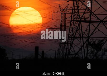 Summer sunset in Greece with electrical pylons near Thessaloniki city. High voltage electricity poles - towers during the sunset time in the magic hour. The metal towers as seen in the sunset in the Greek countryside, distribute electric energy from the power station where electricity is generated in coal production, across the country. The electric wires, the grid and pillars or power pylons are seen as silhouettes in the colorful cloudy dusk evening sky. Oreokastro, Thessaloniki in Greece on July 25, 2021 (Photo by Nicolas Economou/NurPhoto) Stock Photo