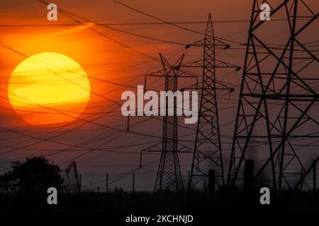 Summer sunset in Greece with electrical pylons near Thessaloniki city. High voltage electricity poles - towers during the sunset time in the magic hour. The metal towers as seen in the sunset in the Greek countryside, distribute electric energy from the power station where electricity is generated in coal production, across the country. The electric wires, the grid and pillars or power pylons are seen as silhouettes in the colorful cloudy dusk evening sky. Oreokastro, Thessaloniki in Greece on July 25, 2021 (Photo by Nicolas Economou/NurPhoto) Stock Photo