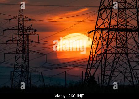 Summer sunset in Greece with electrical pylons near Thessaloniki city. High voltage electricity poles - towers during the sunset time in the magic hour. The metal towers as seen in the sunset in the Greek countryside, distribute electric energy from the power station where electricity is generated in coal production, across the country. The electric wires, the grid and pillars or power pylons are seen as silhouettes in the colorful cloudy dusk evening sky. Oreokastro, Thessaloniki in Greece on July 25, 2021 (Photo by Nicolas Economou/NurPhoto) Stock Photo