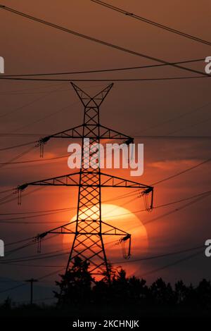 Summer sunset in Greece with electrical pylons near Thessaloniki city. High voltage electricity poles - towers during the sunset time in the magic hour. The metal towers as seen in the sunset in the Greek countryside, distribute electric energy from the power station where electricity is generated in coal production, across the country. The electric wires, the grid and pillars or power pylons are seen as silhouettes in the colorful cloudy dusk evening sky. Oreokastro, Thessaloniki in Greece on July 25, 2021 (Photo by Nicolas Economou/NurPhoto) Stock Photo