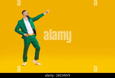 Confident handsome showman in green suit showing pointing on the right on yellow background. Stock Photo