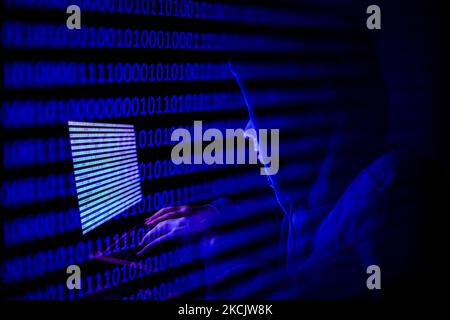 A person dressed as an internet hacker is seen with binary code displayed on a laptop screen in this double exposure illustration photo taken in Krakow, Poland on August 17, 2021. (Photo by Jakub Porzycki/NurPhoto) Stock Photo