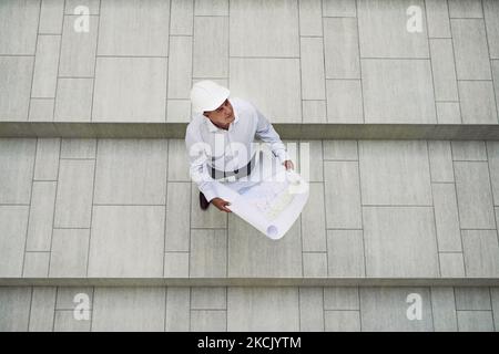 Looking at the potential of the project. High angle shot of a focused professional male architect holding blueprints while looking up inside of a Stock Photo
