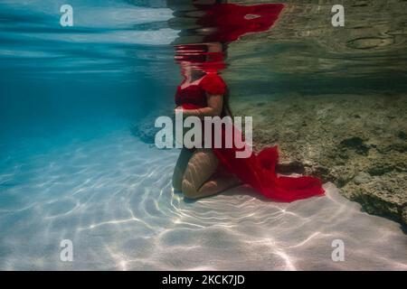 Young pregnant woman showing baby bump for an underwater photo shoot. Stock Photo