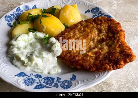 Traditional polish breaded pork chop called kotlet schabowy, salad with cucumbers and sour cream called mizeria and potatoes are seen on the home table in Chocznia on August 28, 2021. (Photo by Jakub Porzycki/NurPhoto) Stock Photo