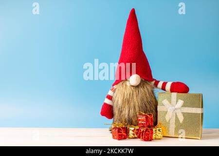 Cute Christmas gnome with gift boxes on blue background. Space for text Stock Photo