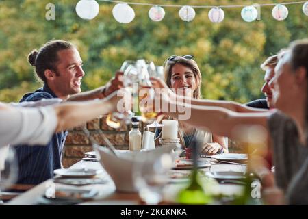 Living the good life with friends. a group of happy young friends toasting with wine at a backyard dinner party. Stock Photo