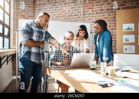 Teamwork simplifies the task. a group of colleagues using a laptop together in a modern office. Stock Photo