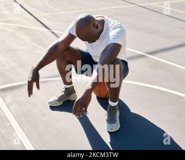 Basketball court, tired and black man sitting on a basketball resting or relaxing on a fitness training or workout break. Loser, wellness and African Stock Photo