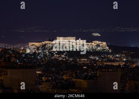 Night view of the Parthenon and Acropolis with a ferry boat passing in the background in the Greek capital Athina. Long exposure photography technique is showing the antiquities illuminated in the dark with the urban landscape of the city around.. The ancient hill of Acropolis, including the worldwide known marble made temple Parthenon and remains of many ancient buildings of great architectural and historic significance as the Erechtheion, Propylaia, Temple of Athena Nike, the Caryads and more. Acropolis was severed heavy damage during the Ottoman occupation. It is nowadays UNESCO World Herit Stock Photo