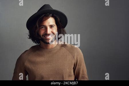 He gets hearts racing when he wears that hat. Studio shot of a handsome young man wearing a hat against a gray background. Stock Photo