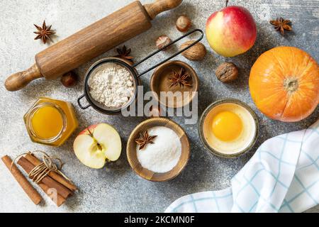 Baking food background. Pumpkins, apples, honey, nuts and seasonal spices for pumpkin or apple pie on a gray tabletop. View from above. Stock Photo