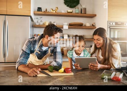 What are we making next. two happy parents and their young daughter trying a new recipe in the kitchen together. Stock Photo