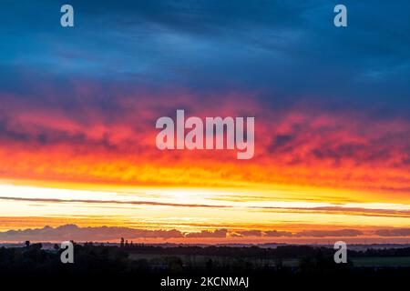 Sunrise over Thanet and the Kent landscape seen from Herne Bay. Winter, with layers of cloud in the sky, underlit by the still to rise sun making them orange and yellow. Stock Photo