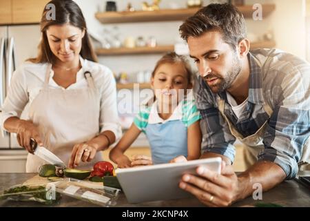 Following the recipe to a T. two happy parents and their young daughter trying a new recipe in the kitchen together. Stock Photo