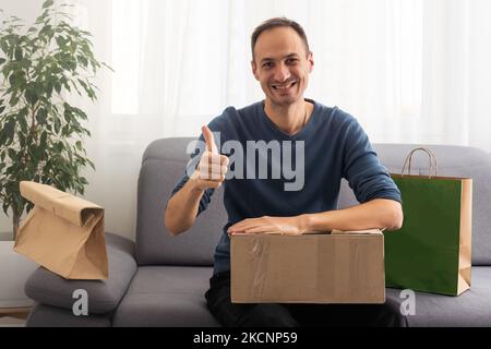 Present from distant friend. Happy millennial man unpack open box with birthday gift surprise received by mail. Smiling young guy has pleasure to Stock Photo