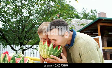 in summer, in the garden, father with a four-year-old son cut a watermelon and eat it, have fun, a boy likes watermelon very much. sweet watermelon for lunch with family. High quality photo Stock Photo