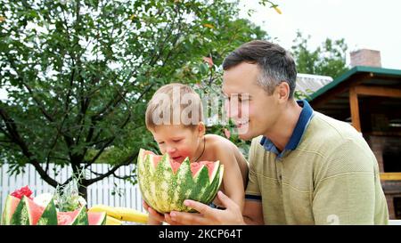 in summer, in the garden, father with a four-year-old son cut a watermelon and eat it, have fun, a boy likes watermelon very much. sweet watermelon for lunch with family. High quality photo Stock Photo