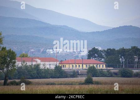 The iconic train station of Idomeni, with houses from villages of N. Macedonia in the background. Asylum Seekers are trying to cross the Greek-North Macedonian borders to follow the Balkan Route, famous in 2015-2016 during the Syrian refugee crisis, from Idomeni, Greece to Gevgelija, North Macedonia following the train rails and railway station and then reach central and northern Europe. Refugees and Migrants are seen walking in the fields in the Greek side, before the fence that separates the two countries, trying to reach and pass the borders. The small groups are mostly male dominated from  Stock Photo