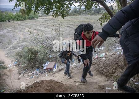 Group of three young asylum seekers walking up to a hill as they return from their attempt to cross the borders. Asylum Seekers are trying to cross the Greek-North Macedonian borders to follow the Balkan Route, famous in 2015-2016 during the Syrian refugee crisis, from Idomeni, Greece to Gevgelija, North Macedonia following the train rails and railway station and then reach central and northern Europe. Refugees and Migrants are seen walking in the fields in the Greek side, before the fence that separates the two countries, trying to reach and pass the borders. The small groups are mostly male  Stock Photo