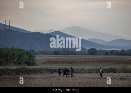 Asylum Seekers are trying to cross the Greek-North Macedonian borders to follow the Balkan Route, famous in 2015-2016 during the Syrian refugee crisis, from Idomeni, Greece to Gevgelija, North Macedonia following the train rails and railway station and then reach central and northern Europe. Refugees and Migrants are seen walking in the fields in the Greek side with the N. Macedonian Mountains in the background, before the fence that separates the two countries, trying to reach and pass the borders. The small groups are mostly male dominated from Afghanistan, newcomers who began their trip aft Stock Photo