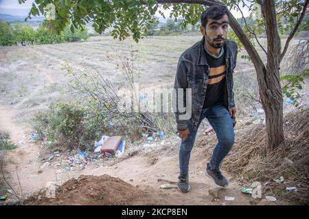 Group of three young asylum seekers walking up to a hill as they return from their attempt to cross the borders. Asylum Seekers are trying to cross the Greek-North Macedonian borders to follow the Balkan Route, famous in 2015-2016 during the Syrian refugee crisis, from Idomeni, Greece to Gevgelija, North Macedonia following the train rails and railway station and then reach central and northern Europe. Refugees and Migrants are seen walking in the fields in the Greek side, before the fence that separates the two countries, trying to reach and pass the borders. The small groups are mostly male  Stock Photo