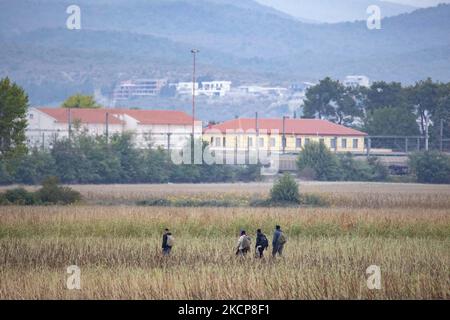 Migrants are seen walking in the fields with the iconic yellow train station of Idomeni and houses in N. Macedonia in the background. Asylum Seekers are trying to cross the Greek-North Macedonian borders to follow the Balkan Route, famous in 2015-2016 during the Syrian refugee crisis, from Idomeni, Greece to Gevgelija, North Macedonia following the train rails and railway station and then reach central and northern Europe. Refugees and Migrants are seen walking in the fields in the Greek side, before the fence that separates the two countries, trying to reach and pass the borders. The small gr Stock Photo