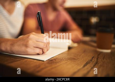 The mind forgets, but the pen remembers. two unidentifiable students having a study session at a cafe table. Stock Photo