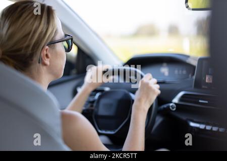 Business woman driving a car to work. Female driver steering car on the road. Stock Photo