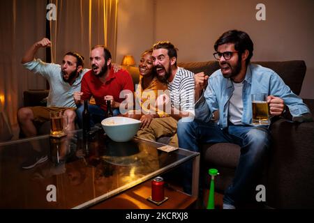 Group of five emotional adult friends watching sports match on tv, celebrating the victory of his team sitting on couch. Sports Concept. Stock Photo