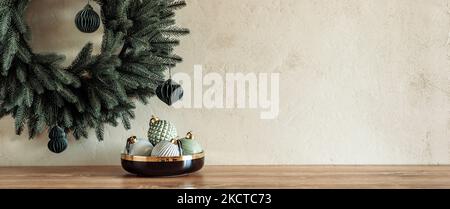 Minimal composition with pastel colored baubles in bowl on table with Christmas wreath on textured stone wall Stock Photo