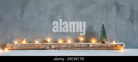 Small Christmas tree with lights on an old wooden plank on a textured gray stone wall background Stock Photo