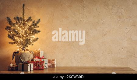 Small Christmas tree with lights and gift boxes on old wooden table on cozy textured stone wall background Stock Photo