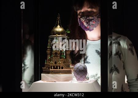 LONDON, UNITED KINGDOM - NOVEMBER 17, 2021: A staff member looks at the Moscow Kremlin Egg – the largest Imperial Egg – inspired by the architecture of the Dormition Cathedral, on loan from the Moscow Kremlin Museums (L) and the Swann Egg (R) during a photocall for the upcoming exhibition 'Faberge in London: Romance to Revolution' at the V&A (20 November 2021 – 8 May 2022), on 17 November, 2021 in London, England. The V&A’s major exhibition with over 200 objects on display including a collection of Imperial Easter Eggs will explore craftsmanship of master Russian goldsmith Carl Faberge and the Stock Photo