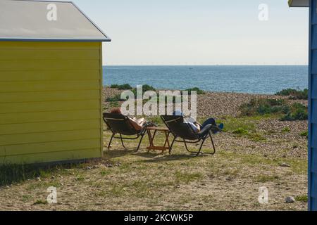 Man and woman couple relaxing in chairs by beach huts on the shingle beach at Littlehampton in West Sussex, England. Unrecognisable people. Stock Photo