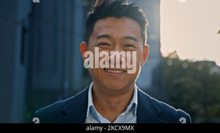 Outdoors portrait Asian 40s mature businessman smiling happy in city in sun lights. Close up glad success cheerful positive middle-aged man business Stock Photo