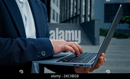 Close up male hands unrecognizable businessman typing laptop outdoors in downtown standing in city unknown entrepreneur employer man worker manager Stock Photo