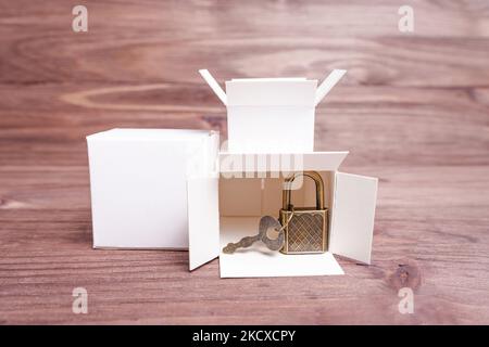 Miniature white shipping boxes and bronze toned keyed padlock isolated on a wooden background. Online shopping safety concept. Stock Photo