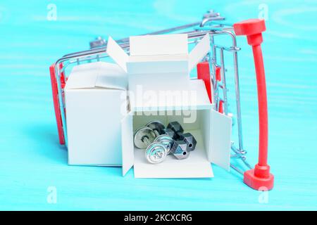 Tiny steel dumbbells in a small shipping box placed in an overturned toy push trolley isolated on a blue wooden background. Order gym equipment online Stock Photo