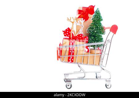 Toy christmas tree, deers and gift boxes packed in a miniature shopping trolley isolated on white. Buying christmas props and presents online. Stock Photo