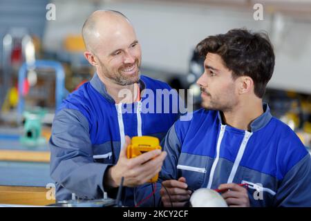 supervisor training apprentice using multimeter in factory Stock Photo