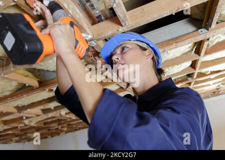female builder using drill on wooden trusses Stock Photo